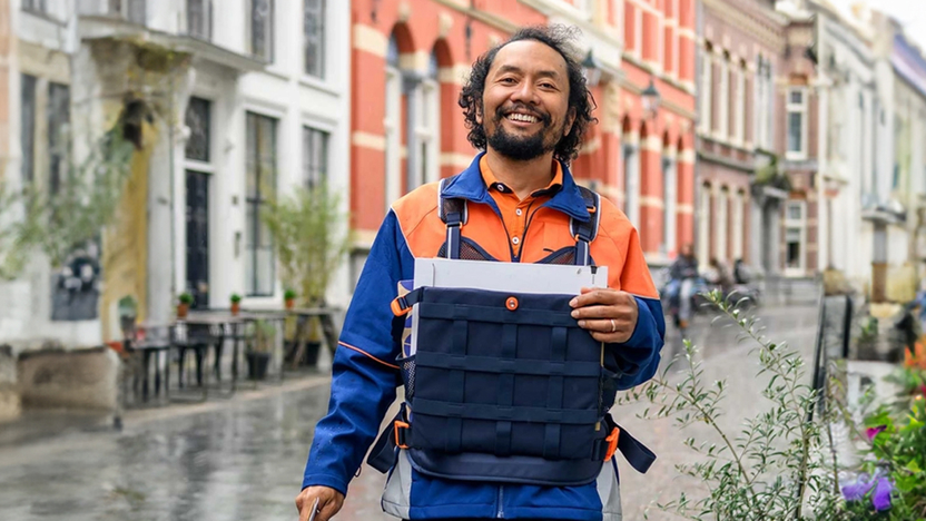 Postbezorger met een tas vol post die vrolijk door de straat loopt | Header bij referentverhaal PostNL